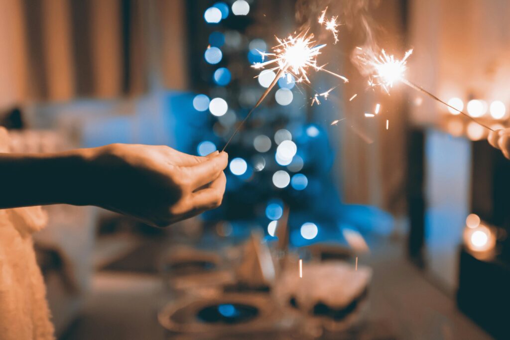 Hands holding sparklers in a festive indoor setting with blurred lights and bokeh effect.