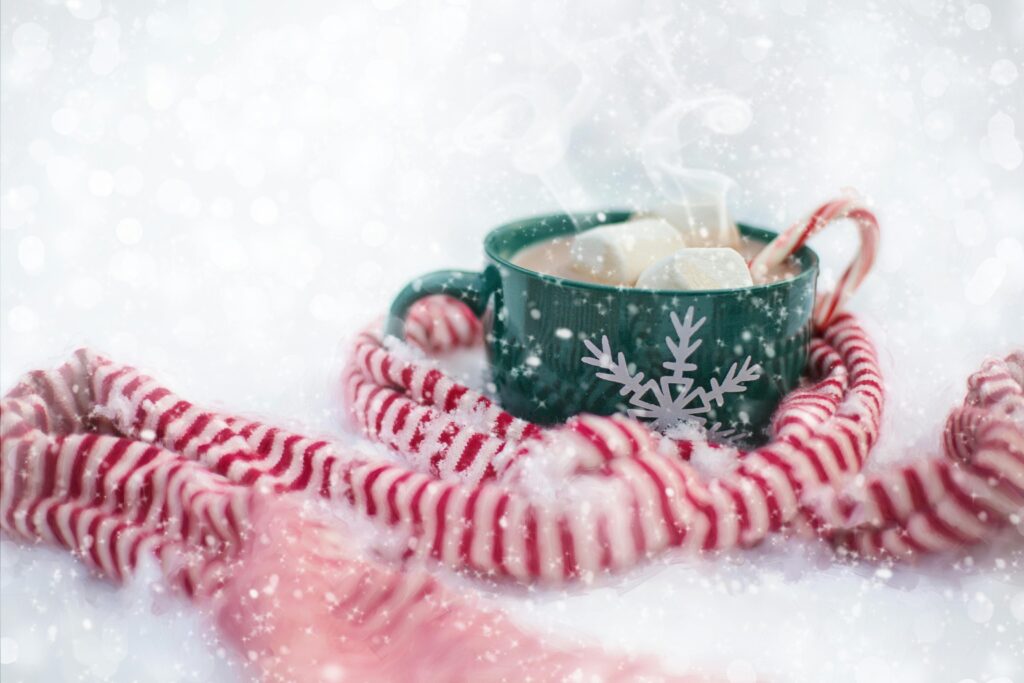 A steaming cup of hot chocolate with marshmallows and candy cane in a snowy setting, perfect for winter coziness.